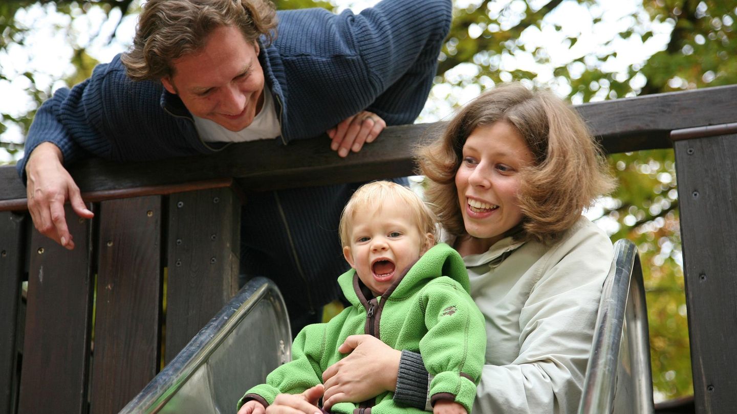 Junge Familie mit Kind auf der Spielplatz-Rutsche