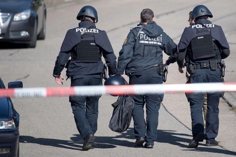 Polizeibeamte gehen in Villingendorf hinter einer Absperrung in der Nähe des Tatorts.