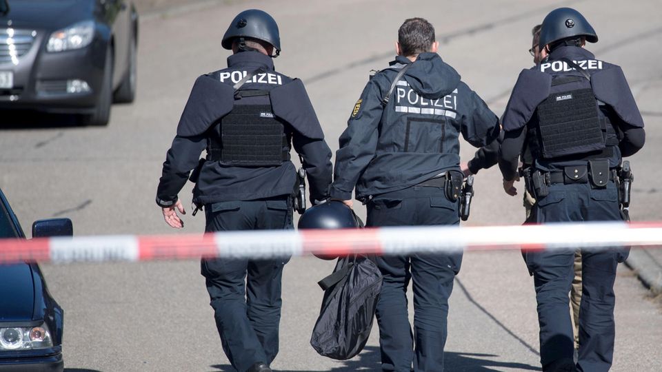 Polizeibeamte gehen in Villingendorf hinter einer Absperrung in der Nähe des Tatorts.