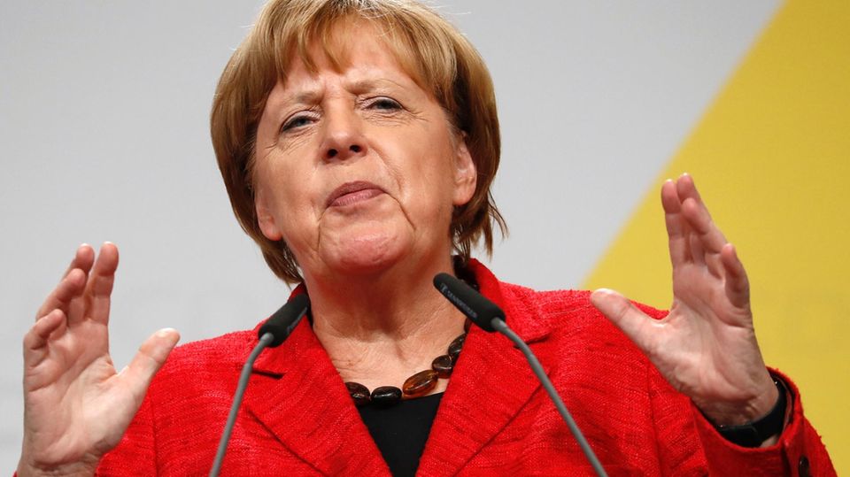 Angela Merkel mit verkniffenem Gesicht, hebt die Hände am Rednerpult