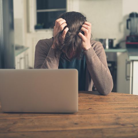 Eine Frau sitzt mit gesenktem Kopf vor ihrem Laptop und rauft sich die Haare