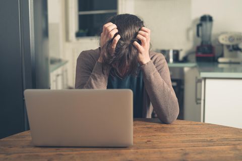 Eine Frau sitzt mit gesenktem Kopf vor ihrem Laptop und rauft sich die Haare