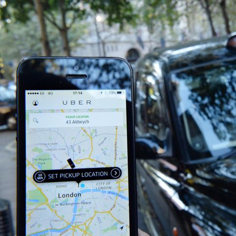 Ein Smartphone-User hat die Uber App geöffnet, im Hintergrund eins schwarzes Taxi aus London