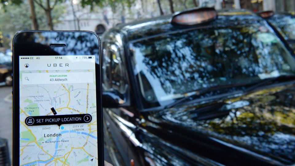 Ein Smartphone-User hat die Uber App geöffnet, im Hintergrund eins schwarzes Taxi aus London