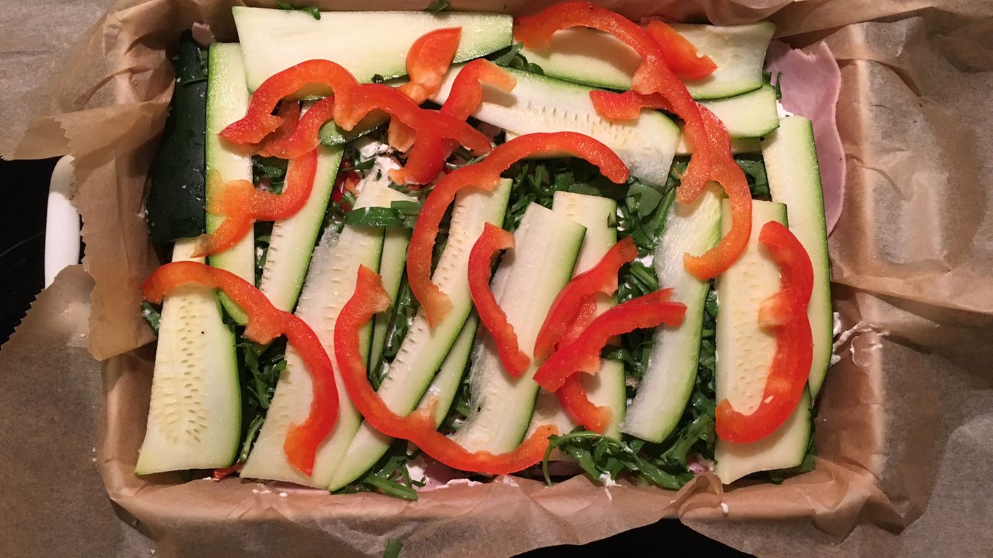 Für die Gemüse-Lasagne heißt es zunächst einmal: schnippeln. In der Auflaufform landen 500 Gramm Zucchini, 75 Gramm Rucola, eine Knoblauchzehe, etwas Chili, eine rote Paprika, 100 Gramm Ricotta, 200 Gramm Schinken, Kräuter der Provence, Salz, Pfeffer, 30 Gramm Parmesan  - und eine halbe Packung "Good Eggwhites". Das entspricht etwa 250 Gramm Hühner-Eiweiß.  Laut Rezept soll das Schneiden und Schichten der Zutaten etwa 15 Minuten dauern. Das ist für unseren Test etwas zu knapp bemessen: Weil die Zucchini in feine Scheiben geschnitten werden müssen, dauert es ein paar Minuten länger.