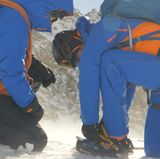 Wir legen die Steigeisen an. Einfach gesagt, schwer getan. Ein elendes Gefummel bei eisiger Kälte, Wind und Handschuhen. Doch die Dinger müssen bombenfest am Stiefel sitzen, sonst wird es gefährlich. 