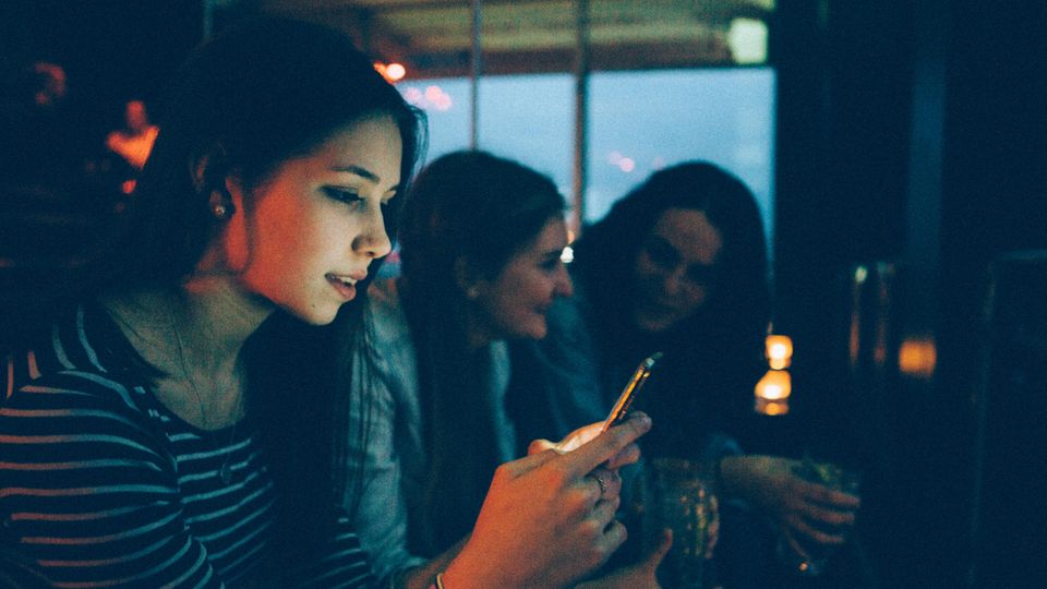 Eine Frau sitzt in einer Bar und hängt am Handy