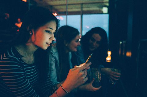 Eine Frau sitzt in einer Bar und hängt am Handy