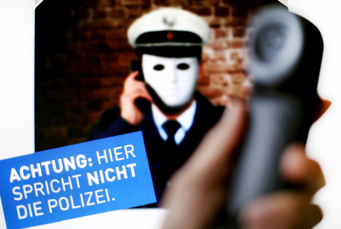 Ein Telefonhörer vor einem Plakat der Polizei NRW mit der Aufschrift "Achtung: Hier spricht nicht die Polizei"
