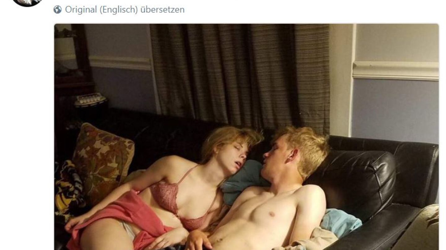 Ein junger Mann liegt mit nacktem Oberkörper und karierter Pyjamahose schlafend auf einer Couch, seine Freundin neben ihm
