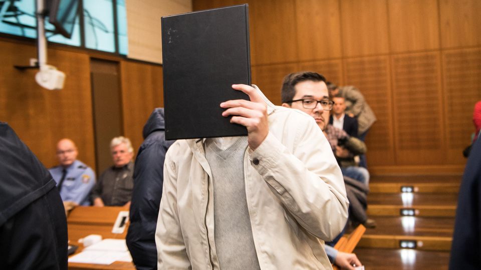 Prozessbeginn in Frankfurt: Der Angeklagte hält sich eine Mappe vors Gesicht Prozessbeginn in Frankfurt: Der Angeklagte hält sich eine Mappe vors Gesicht