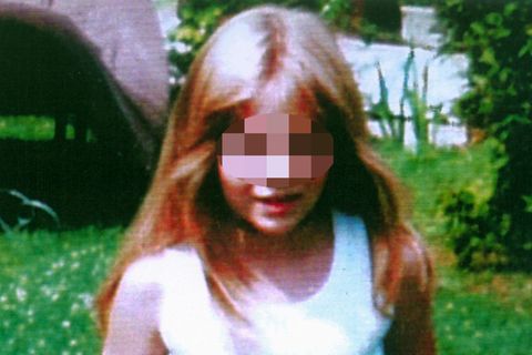 Johanna, ein achtjähriges, blondes Mädchen mit weißem Top und roter Hose steht auf einem Rasen mit Gänseblümchen