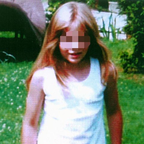 Johanna, ein achtjähriges, blondes Mädchen mit weißem Top und roter Hose steht auf einem Rasen mit Gänseblümchen
