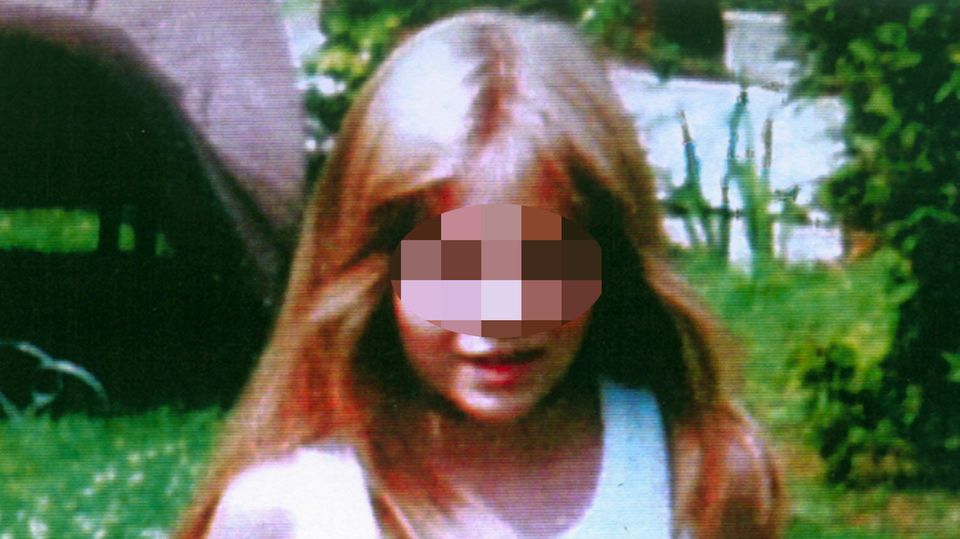 Johanna, ein achtjähriges, blondes Mädchen mit weißem Top und roter Hose steht auf einem Rasen mit Gänseblümchen