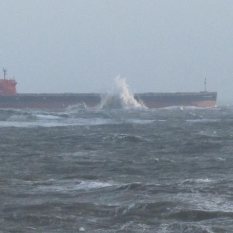 Mit einem Schlepper vor dem Bug liegt der Frachter Glory Amsterdam vor Langeoog auf Grund. An der Bordwand spritzt ein Brecher.