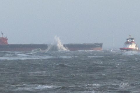 Mit einem Schlepper vor dem Bug liegt der Frachter Glory Amsterdam vor Langeoog auf Grund. An der Bordwand spritzt ein Brecher.