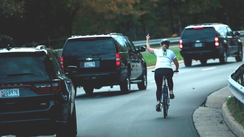 Eine Radfahrerin wird von Donald Trumps Auto-Konvoi überholt und zeigt einen Stinkefinger