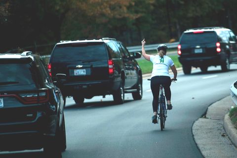 Eine Radfahrerin wird von Donald Trumps Auto-Konvoi überholt und zeigt einen Stinkefinger
