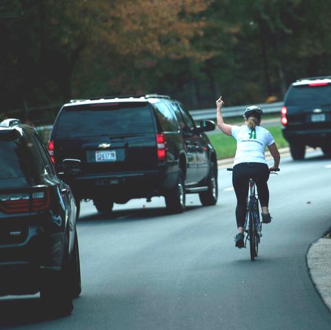 Eine Radfahrerin wird von Donald Trumps Auto-Konvoi überholt und zeigt einen Stinkefinger