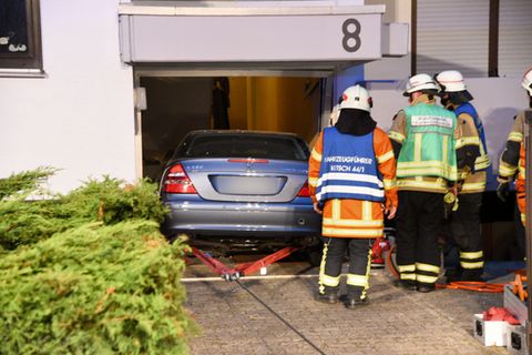Drei Feuerwehrleute schauen zu, während ein Mercedes rückwärts aus einem demolierten Hauseingang gezogen wird