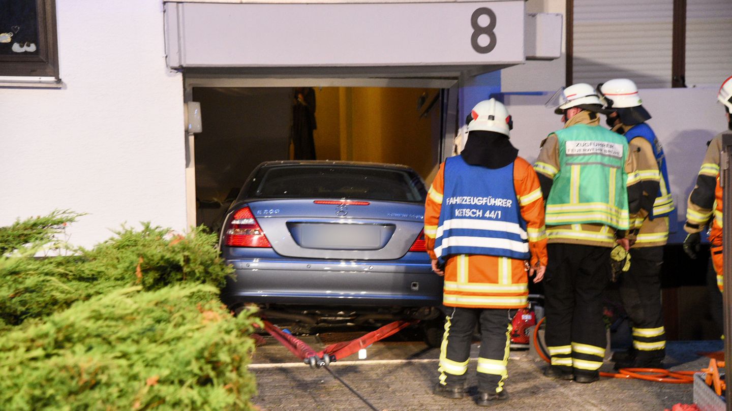 Drei Feuerwehrleute schauen zu, während ein Mercedes rückwärts aus einem demolierten Hauseingang gezogen wird