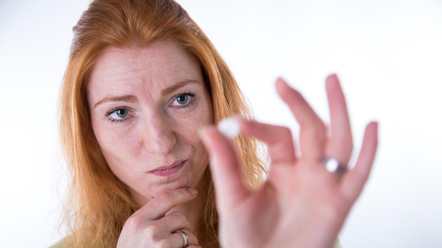 Eine Frau betrachtet skeptisch die Pille