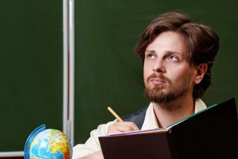 Mann sitzt an einem Lehrerpult vor einer Tafel