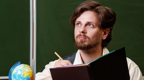 Mann sitzt an einem Lehrerpult vor einer Tafel