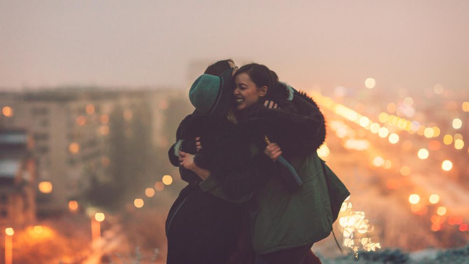 Drei Freundinnen stehen auf einer Brücke und umarmen sich