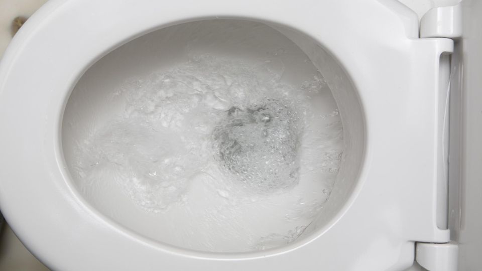 Eine Toilettenschüssel von oben, in der gerade die Spülung betätigt wurde. Durch die Klobrille hindurch sieht man Wasserwirbel