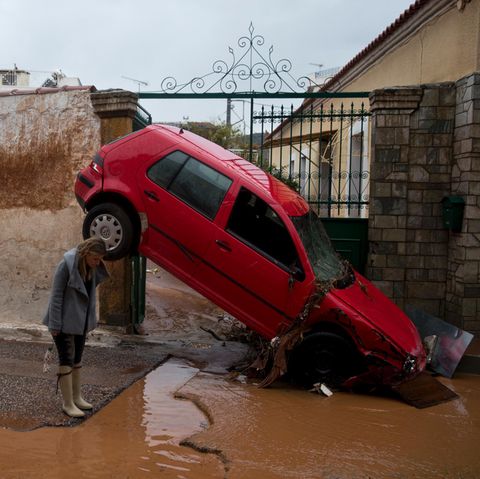 Eine Frau steht im griechischen Mandra vor einem von den Überschwemmungen beschädigten Auto