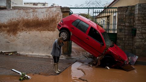 Eine Frau steht im griechischen Mandra vor einem von den Überschwemmungen beschädigten Auto