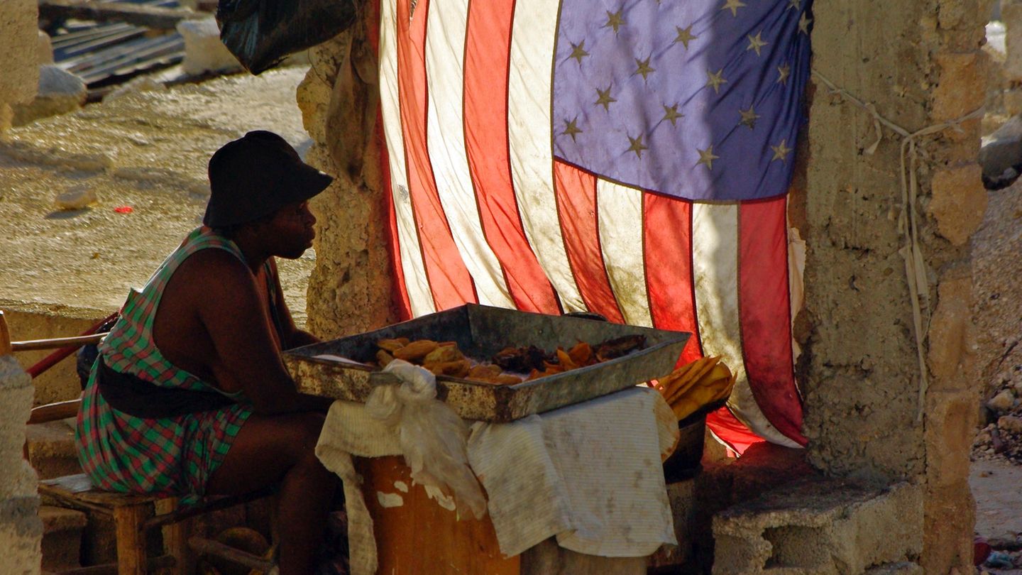 Frau sitzt in Port-au-Prince neben einer Flagge der USA