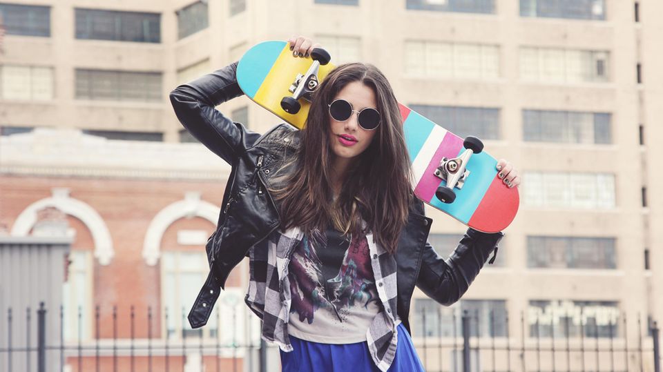 Eine junge Frau mit Sonnenbrille trägt ein Skateboard
