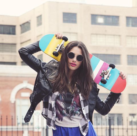 Eine junge Frau mit Sonnenbrille trägt ein Skateboard