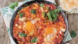 Shakshuka      Zutaten für 4 Personen:  2 Zwiebeln, 4 Knoblauchzehen, 2 rote Paprikaschoten, 1 TL Kreuzkümmelsamen, 1 TL Koriandersamen, 4 EL Olivenöl, 1 Dose Flaschentomaten (etwa 400 g), 1 Dose Cocktailtomaten (etwa 400 g), Salz, frisch gemahlener schwarzer Pfeffer, 1/2 Bund frischer Koriander, 4-8 Eier (pro Person 1-2 Eier), 150 g Feta    Außerdem: frisches Fladenbrot      Zubereitung:  Zwiebeln sowie Knoblauch abziehen und fein würfeln. Die Paprika waschen, trockentupfen, von Stielansätzen und Samen befreien und ebenfalls klein schneiden.  Die Kreuzkümmel- und Koriandersamen in einer Pfanne ohne Fett rösten, bis die Gewürze duften. Im Mörser fein zerreiben.  In einer großen oder zwei kleineren Pfannen das Olivenöl bei mittlerer Temperatur erhitzen. Die Zwiebeln und den Knoblauch darin anschwitzen, bis die Zwiebeln glasig sind. Die Paprika zugeben und 2-3 Minuten mitbraten. Die Tomaten in die Pfanne geben und mit dem Kochlöffel zerdrücken. Kräftig mit Salz, Pfeffer, gemahlenem Kreuzkümmel sowie Koriander würzen und die Mischung etwa 15 Minuten einköcheln lassen.   Den frischen Koriander waschen und trockenschütteln. Die Hälfte des Korianders hacken und unter die Tomaten rühren, von der anderen Hälfte die Blätter abzupfen und beiseitelegen.  Mit dem Kochlöffel Vertiefungen in die Sauce drücken und die Eier hineinschlagen. den Feta zerbröseln und auf den Tomaten um die Eier herum verteilen. Die Eier bei mittlerer Temperatur stocken lassen, bis das Eiweiß fest ist.  Salzen, pfeffern und mit Korianderblättern bestreut in der Pfanne servieren. Dazu passt frisches Fladenbrot. 