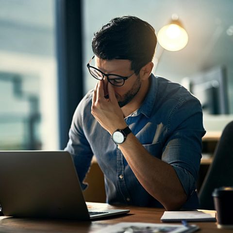 Ein Mann mit Brille sitzt vor dem Laptop und massiert sich die Nase