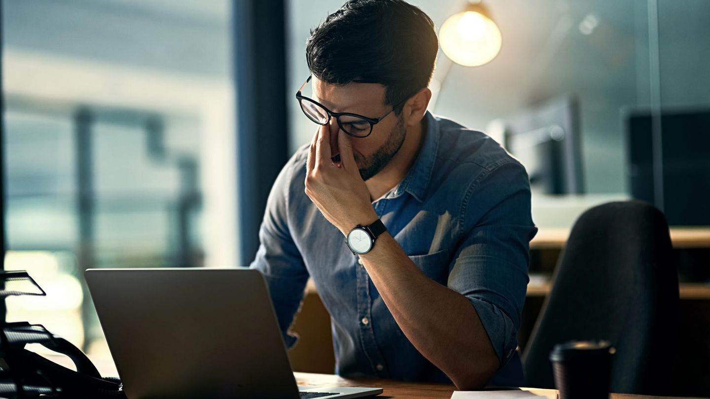 Ein Mann mit Brille sitzt vor dem Laptop und massiert sich die Nase