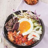 Bibimbap: koreanische Bowl        Zutaten:    Für das Fleisch und die Marinade: 2 Knoblauchzehen, 3 EL Sojasauce, 1 EL Honig, 1 EL Sesamöl, 1 TL Sesamsaat, 250 g Lendensteak vom Rind,     Für das Gemüse: 1/3 Salatgurke, 1 TL Sesamöl, 2 EL Reisessig, Salz, 2 Mairübchen oder 1/2 weißer Rettich, 1 Chilischote, gehackt, 2 EL Weißweinessig, 1 EL Sonnenblumenöl Für den Kimchi: 200 g Chinakohl, Salz, 1 TL brauner Zucker, 1 EL Sojasauce, 1 EL Chilipaste,     Außerdem: 250 g Basmati-Reis, 1 rote Paprikaschote, 1 Knoblauchzehe, 1 Frühlingszwiebel, 3 EL Sonnenblumenöl, Salz, 2 Handvoll Sojasprossen, 4 Eier        Zubereitung:    Für die Rindfleisch-Marinade die Knoblauchzehen abziehen und hacken. Mit Sojasauce, Honig, Sesamöl sowie Sesamsaat vermengen und das Rindfleisch in einem Plastikbeutel oder einer Schüssel über Nacht darin marinieren.    Für das Gemüse die Gurke waschen und in mundgerechte Stücke schneiden. Mit Sesamöl, Reisessig und 1/2 TL Salz über Nacht marinieren. Die Mairübchen schälen und in dicke Stifte schneiden. Mit Chili, 1/2 TL Salz, Weißweinessig und Sonnenblumenöl mischen, über Nacht marinieren. Für den schnellen Kimchi den Chinakohl putzen und mundgerecht schneiden. Mit 1 EL Salz, dem braunen Zucker, Sojasauce und Chilipaste gut durchkneten. Mindestens über Nacht durchziehen lassen.    Am Zubereitungstag den Reis mit der doppelten Menge Wasser bissfest garen. Währenddessen die Paprika waschen, abtupfen, von Stielsatz sowie Samen befreien und würfeln, den Knoblauch abziehen und hacken, die Frühlingszwiebel putzen und dünn schneiden.    In einer Pfanne 1 EL Öl erhitzen. Paprika und Knoblauch darin kurz scharf anbraten, salzen und warm stellen.    Anschließend die Sojasprossen scharf anbraten, salzen und ebenfalls warm stellen.  Das Fleisch aus der Marinade nehmen, auf jeder Seite scharf anbraten und aufschneiden. In einer zweiten Pfanne im übrigen Öl die Spiegeleier braten. Alles miteinander anrichten. 