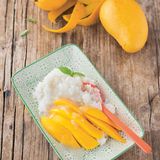 Sticky Rice mit Mango      Zutaten:    200 g Milchreis (alternativ ein anderer Rundkornreis), Salz, 2 Dosen Kokoscreme (800 ml), 60 g Zucker, 1 TL Speisestärke, 2 reife Thai-Mangos, 8–12 Blätter Thai-Basilikum      Zubereitung:    Den Reis unter fließendem kaltem Wasser waschen. Mit der dreifachen Menge Wasser und einer Prise Salz in einem Topf oder Reiskocher zum Kochen bringen, den Deckel auflegen und auf geringster Temperatur gar quellen lassen.        Währenddessen die feste Kokoscreme (die Milch darunter kann für andere Zubereitungen verwendet werden) in einem kleinen Topf mit dem Zucker und etwas Salz bei geringer Temperatur erwärmen. Von der warmen Kokoscreme 2 /3 unter den noch warmen Reis rühren.        Die Speisestärke in 3 EL kaltem Wasser auflösen und unter die übrige Kokoscreme rühren, einmal auf - kochen und andicken lassen. Die Mangos schälen und das Fruchtfleisch vom Kern schneiden, in Spalten schneiden. Thai-Basilikum waschen und trockenschütteln.        Zum Anrichten die Mango auf dem Reis anrichten, mit Kokossauce beträufeln und mit Thai-BasilikumBlättchen dekoriert servieren.