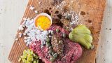 Beef Tatar      Zutaten:    600 g Rinderschulter, 2 Schalotten, 8 Essiggurken, 1 EL Worcester-Sauce, Fleur de Sel, frisch gemahlener schwarzer Pfeffer, 4 Eigelb, 2 EL Kapern aus dem Glas, 2 EL grober Senf,    Außerdem: glatte Petersilie für die Dekoration, frisches Bauernbrot      Zubereitung:  Für das Tatar das frische Fleisch sofort zubereiten und unverzüglich verzehren. Von Silberhäuten, Sehnen und Fett befreien. Zunächst in dünne Scheiben, dann in Streifen und feine Würfel schneiden und zum Schluss hacken.        Die Schalotten abziehen und fein würfeln. Die Hälfte der Gurken ebenfalls fein würfeln und die anderen Gurken dünn auffächern.        Zum Servieren aus dem Fleisch entweder einen großen oder vier kleine, gleich große Laibe formen und auf einem Holzbrett platzieren. Mit Worcester-Sauce beträufeln und mit Salz und Pfeffer würzen. Eigelb (Serviervorschlag: in halben Eierschalen), Zwiebelwürfel, Gurkenwürfel, Gurkenfächer, Kapern und Senf dazu anrichten. Die Petersilie waschen, trockenschütteln, die Blätter abzupfen und das Brett damit dekorieren.    Dazu passt frisches Bauernbrot.