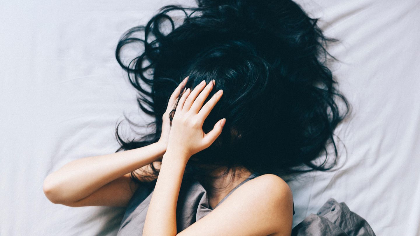 Eine Frau liegt im Bett und hält sich verzweifelt die Hände vor das Gesicht