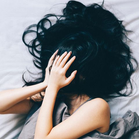 Eine Frau liegt im Bett und hält sich verzweifelt die Hände vor das Gesicht