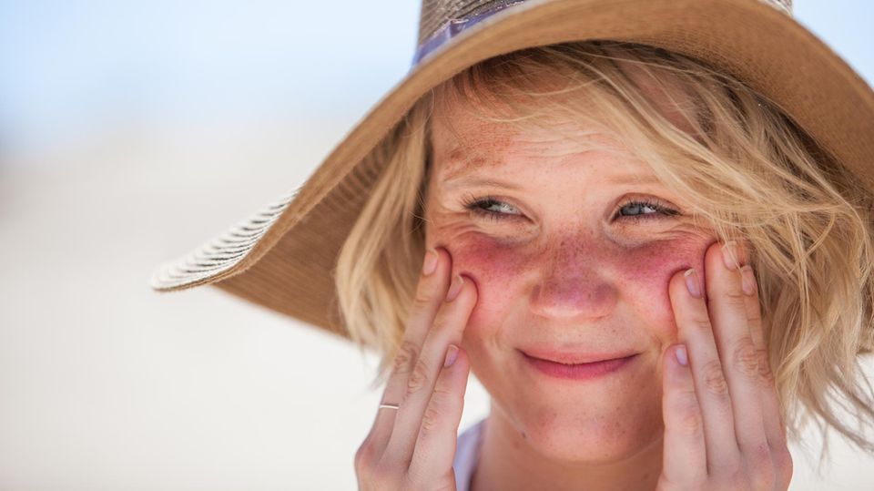 Eine Frau mit Sonnenhut cremt sich mit Sonnencreme die Wangen ein