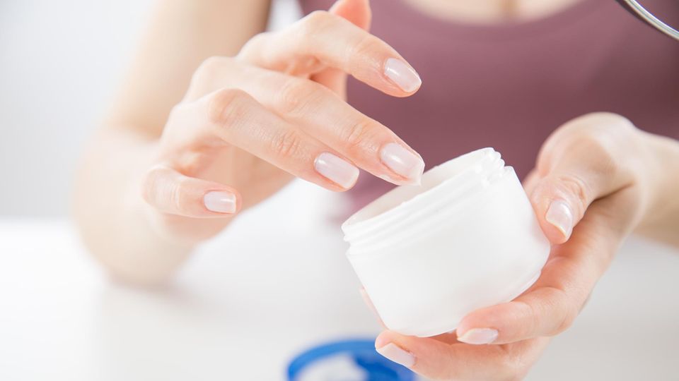 Eine Frau taucht den Finger in einen Tiegel Anti-Falten-Creme