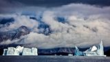 Unterwegs im grönländischen Scoresbysund, dem längsten Fjordsystem der Welt. Im Wasser treiben mächtige Eisberge. Sie sind nicht ungefählich, lugen doch nur ihre Spitzen aus dem Wasser, während der größte Teil unter der Oberfläche lauert, was bekanntermaßen zu Fehleinschätzungen führen kann.