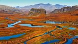 Herbst in Schwedisch-Lappland: Das Flussdelta des Rapaälven mit seinen weit verzweigten Flussläufen erstrahlt in bunten Farben, im Bildzentrum der markante Felsklotz Nammatj. Die Berge im Hintergrund gehören bereits zum Nationalpark Sarek.