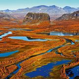 Herbst in Schwedisch-Lappland: Das Flussdelta des Rapaälven mit seinen weit verzweigten Flussläufen erstrahlt in bunten Farben, im Bildzentrum der markante Felsklotz Nammatj. Die Berge im Hintergrund gehören bereits zum Nationalpark Sarek.