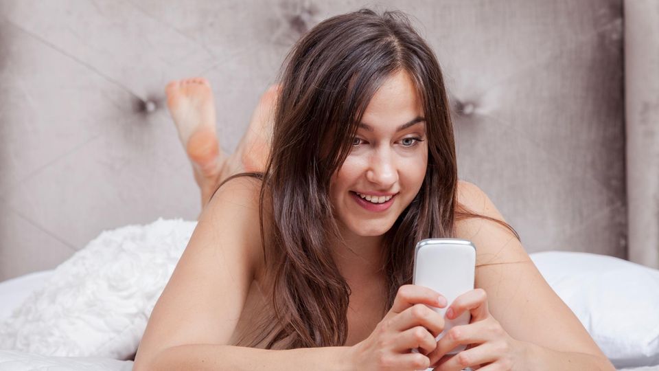 Eine Frau liegt auf dem Bett und hat ein Handy in der Hand