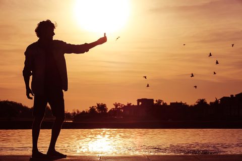 Ein junger Mann steht im Sonnenuntergang am Wasser